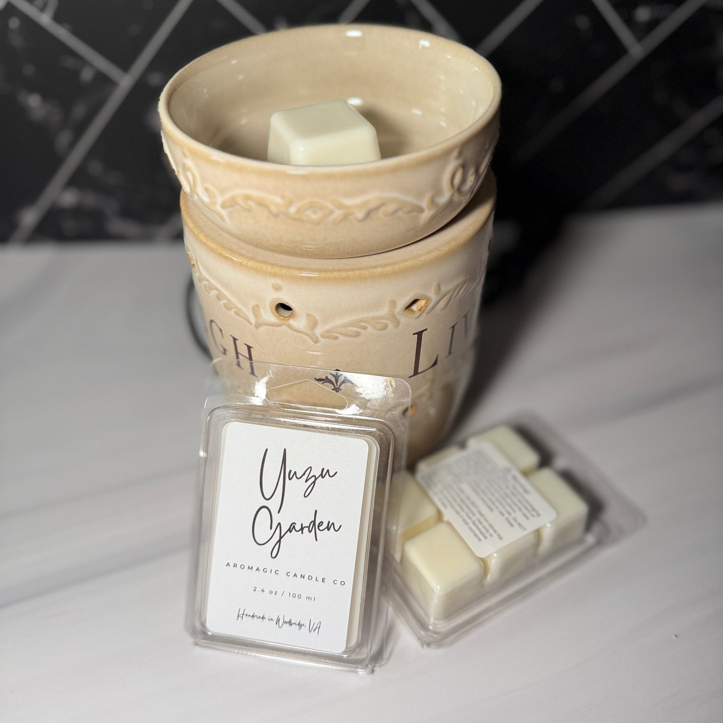 A ceramic wax warmer with a scented wax block and packaging labeled 'Yuzu Garden' on a marble surface.