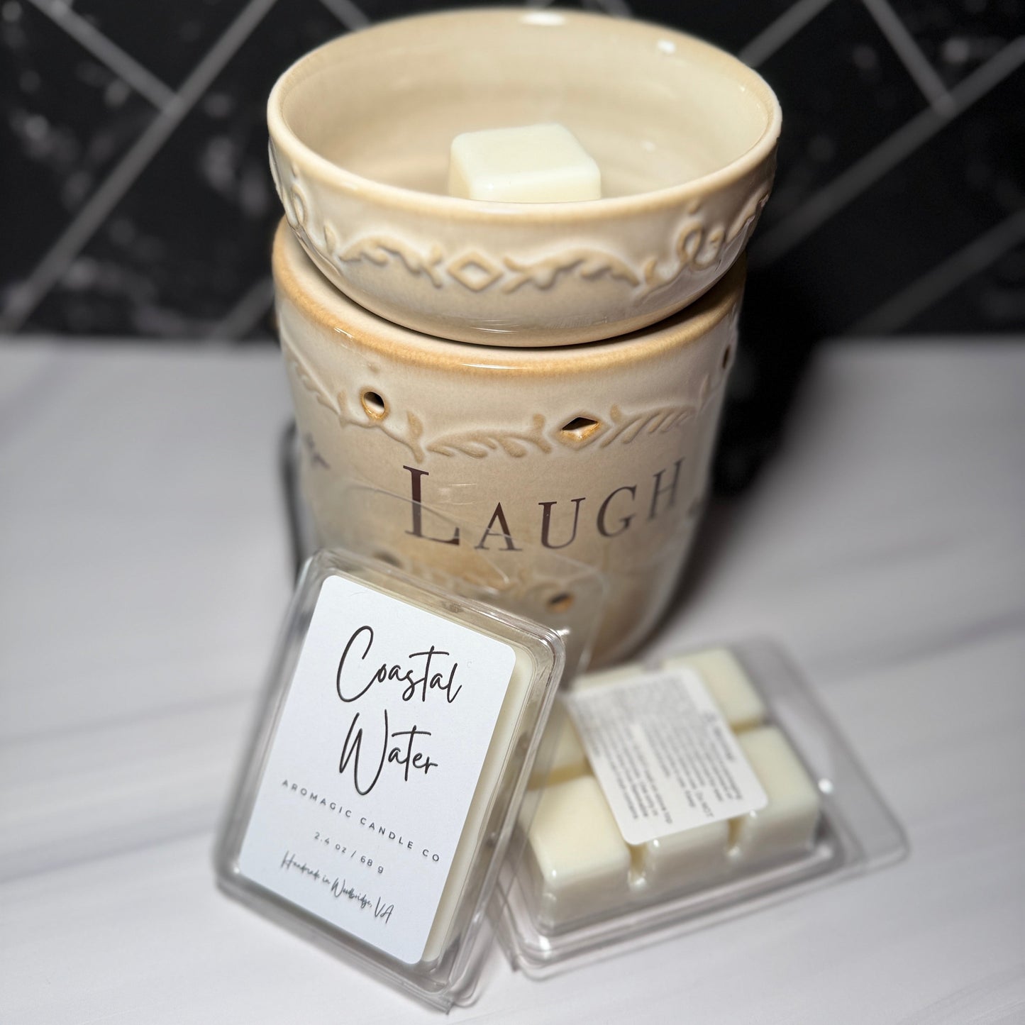 Decorative wax warmer with 'Laugh' text and two wax melts labeled 'Coastal Water' on a marble surface.