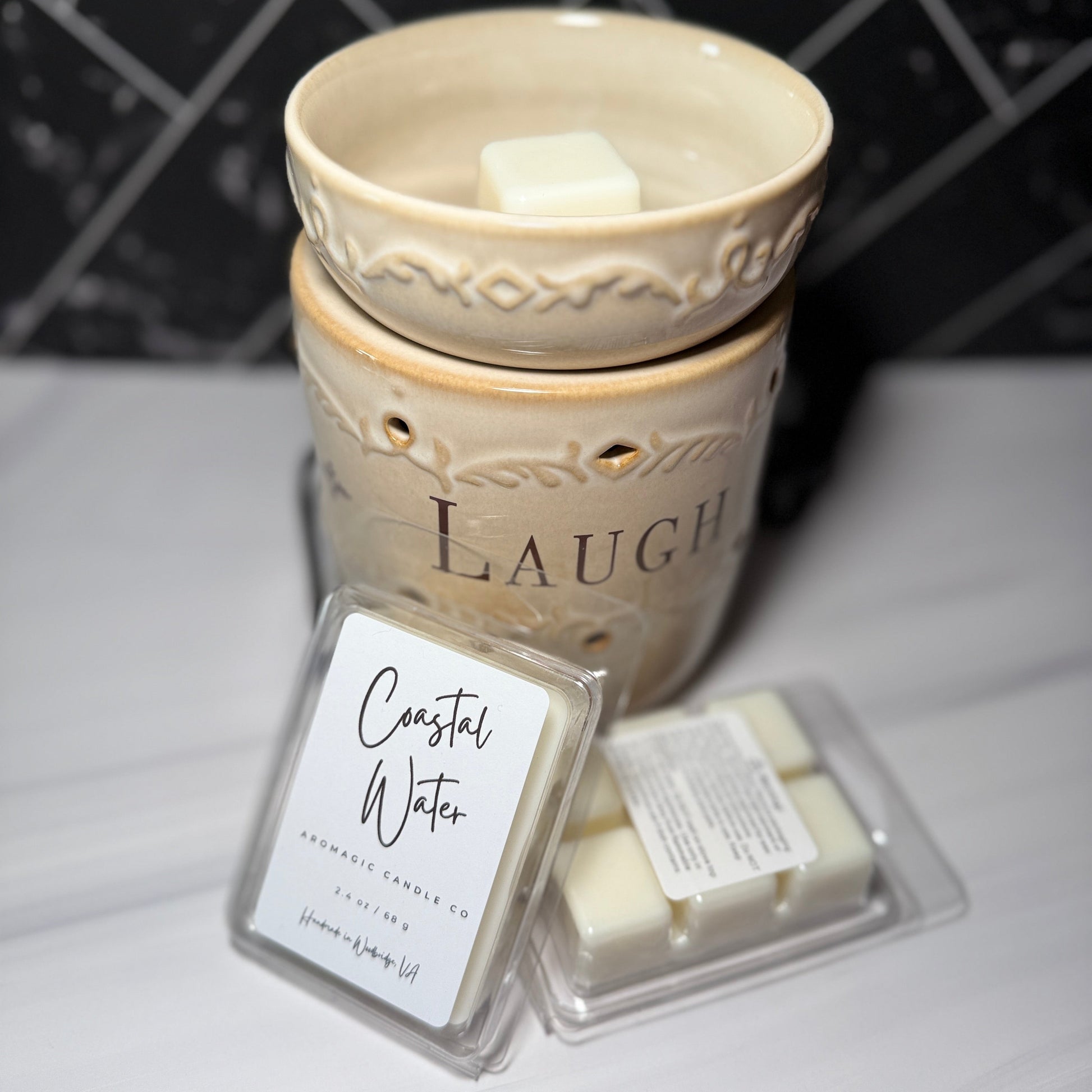 Decorative wax warmer with 'Laugh' text and two wax melts labeled 'Coastal Water' on a marble surface.