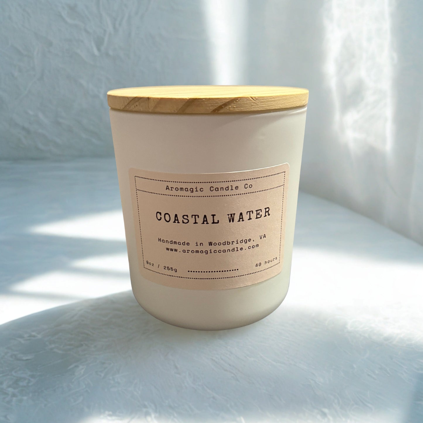 Candle labeled 'Coastal Water' with a wooden lid on a light surface.