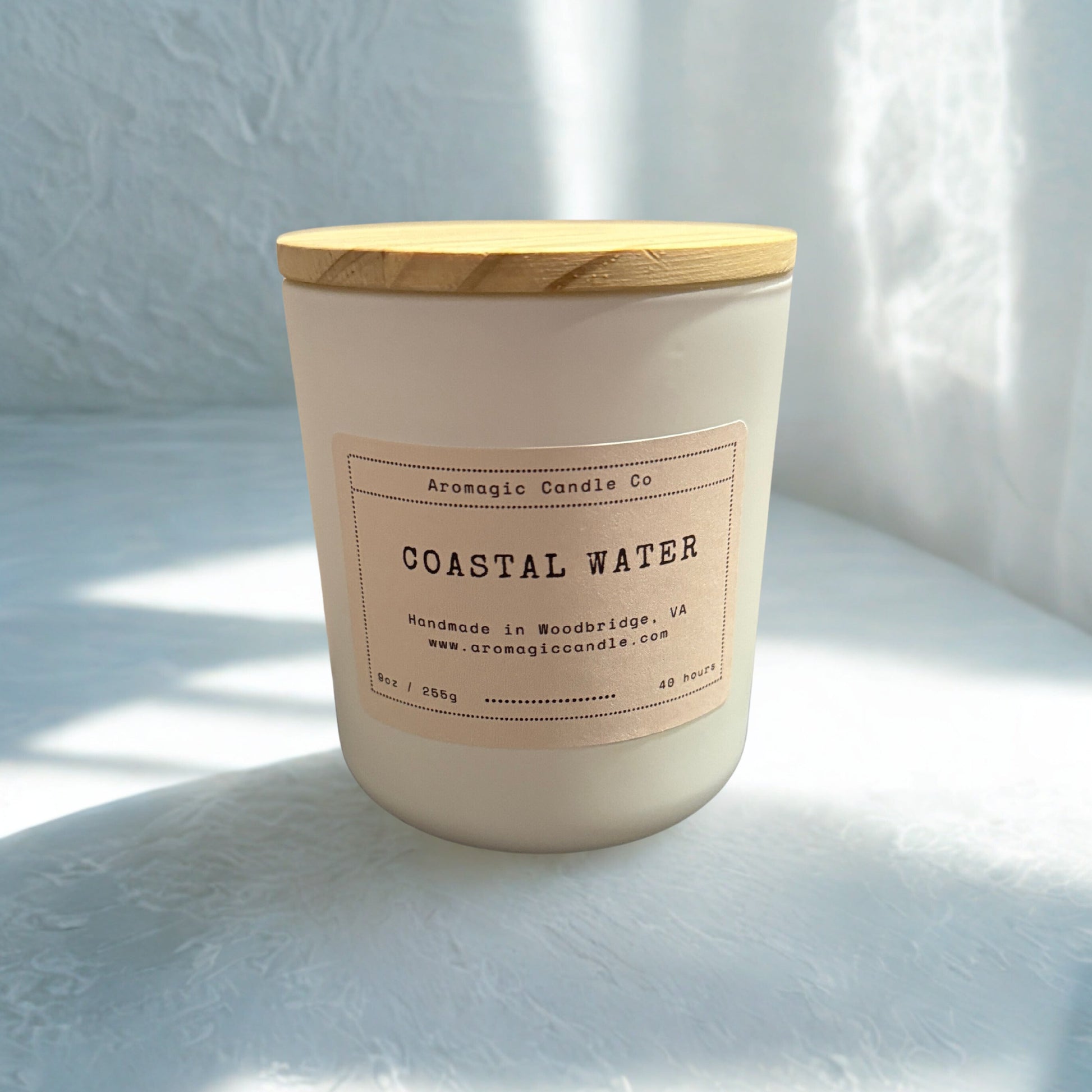 Candle labeled 'Coastal Water' with a wooden lid on a light surface.