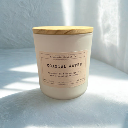 Candle labeled 'Coastal Water' with a wooden lid on a light surface.