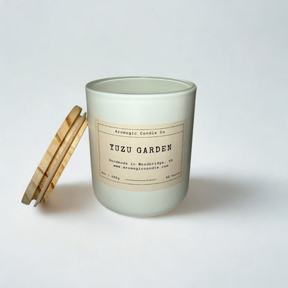 Candle with a wooden lid labeled 'Yuzu Garden' on a white background